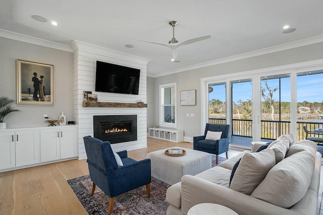 living room with a fireplace, ceiling fan, light wood-style floors, and ornamental molding