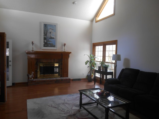 living area featuring visible vents, a brick fireplace, wood finished floors, and vaulted ceiling