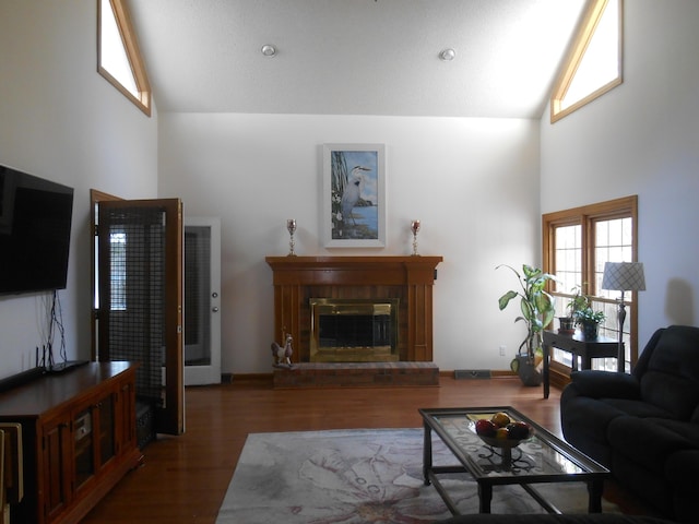 living area with a glass covered fireplace, high vaulted ceiling, visible vents, and wood finished floors