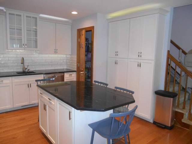 kitchen featuring a breakfast bar, a sink, backsplash, stainless steel dishwasher, and light wood finished floors