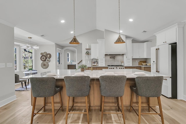 kitchen with visible vents, high end fridge, a sink, custom range hood, and light wood-style floors