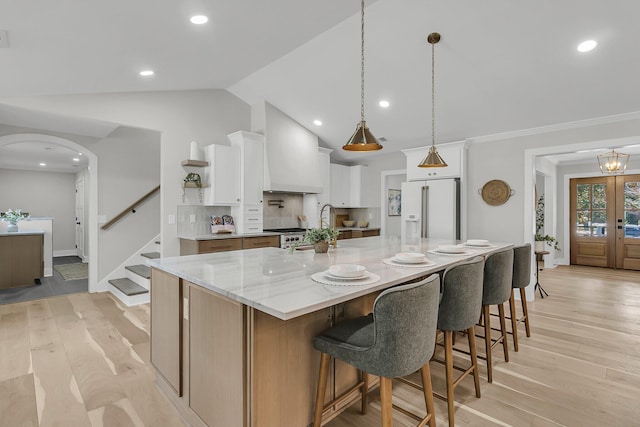 kitchen with light wood-style flooring, custom range hood, white cabinetry, high end white fridge, and arched walkways