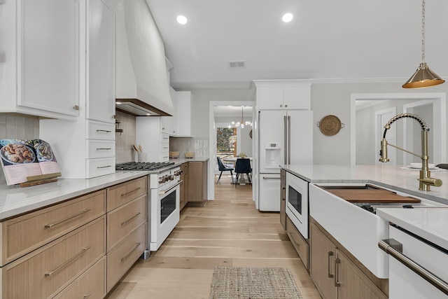 kitchen with white appliances, visible vents, custom exhaust hood, decorative light fixtures, and light wood-type flooring