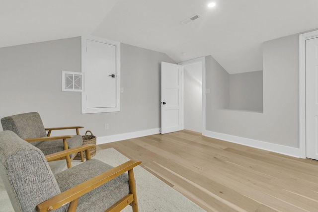 living area featuring lofted ceiling, light wood-style flooring, baseboards, and visible vents