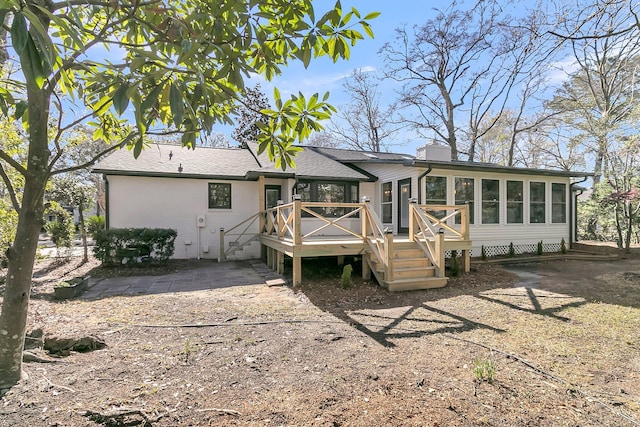 back of house featuring brick siding, a wooden deck, roof with shingles, a chimney, and a sunroom