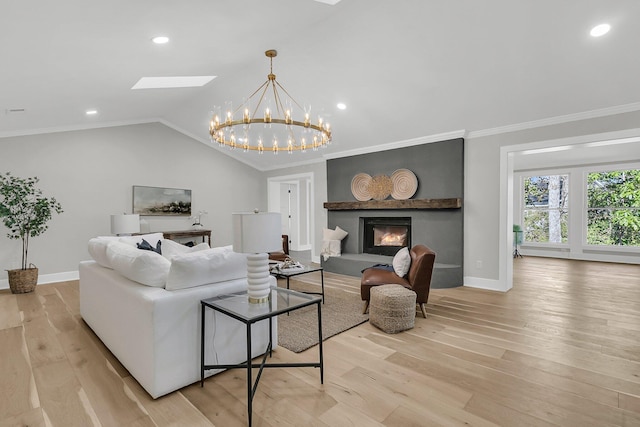 living area featuring a glass covered fireplace, vaulted ceiling with skylight, light wood-style flooring, and ornamental molding