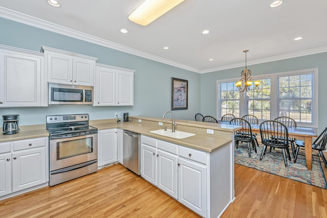 kitchen featuring kitchen peninsula, ornamental molding, stainless steel appliances, white cabinets, and a chandelier