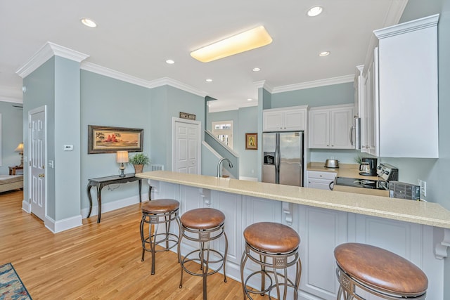 kitchen with a kitchen bar, appliances with stainless steel finishes, ornamental molding, white cabinets, and light hardwood / wood-style floors