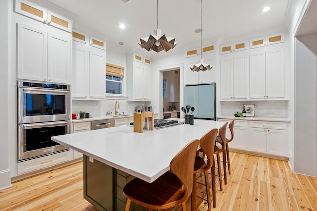 kitchen with appliances with stainless steel finishes, decorative backsplash, a kitchen island, light wood-style flooring, and light countertops