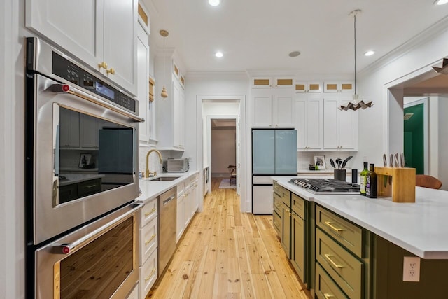 kitchen featuring appliances with stainless steel finishes, white cabinets, light countertops, light wood-style floors, and ornamental molding
