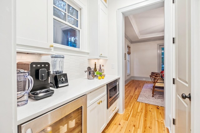 kitchen with stainless steel microwave, ornamental molding, white cabinets, decorative backsplash, and light wood-type flooring