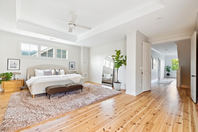 bedroom with light wood-style flooring, a tray ceiling, ornamental molding, ceiling fan, and baseboards