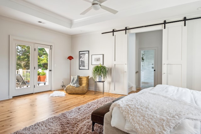 bedroom featuring a barn door, access to exterior, wood finished floors, ornamental molding, and a raised ceiling