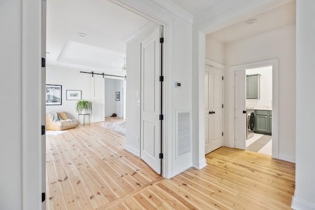 hallway with washer / dryer, light wood finished floors, a barn door, and baseboards