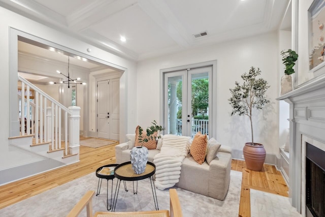 living area featuring hardwood / wood-style floors, a fireplace with flush hearth, stairway, a chandelier, and beam ceiling