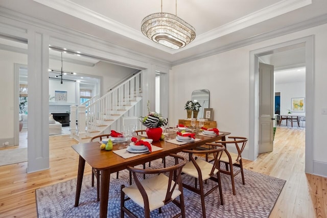 dining area featuring light wood-type flooring, stairs, ornamental molding, a chandelier, and a fireplace