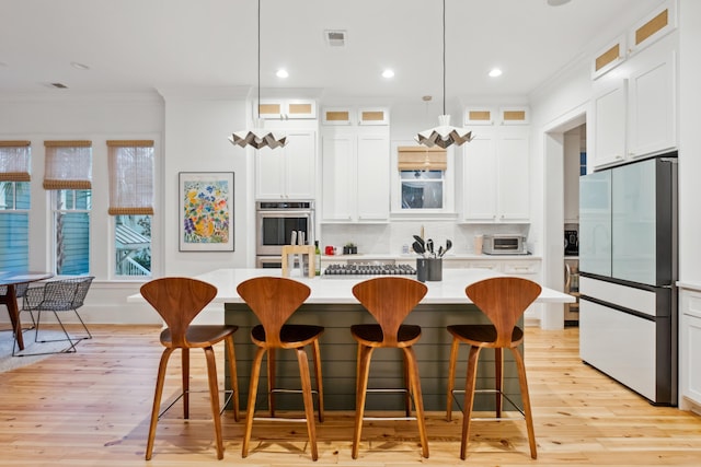 kitchen with fridge, crown molding, light countertops, a kitchen island, and light wood-type flooring