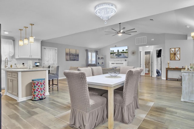 dining area featuring lofted ceiling, sink, ceiling fan with notable chandelier, and light hardwood / wood-style floors