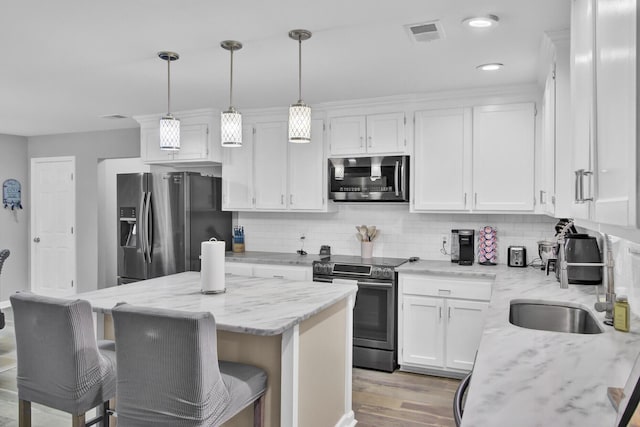 kitchen with decorative light fixtures, white cabinets, a center island, light stone counters, and stainless steel appliances