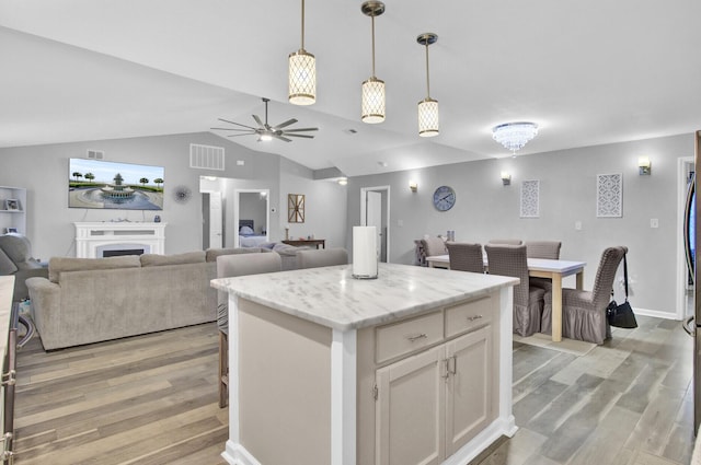 kitchen with light stone counters, light hardwood / wood-style flooring, hanging light fixtures, a kitchen island, and white cabinets