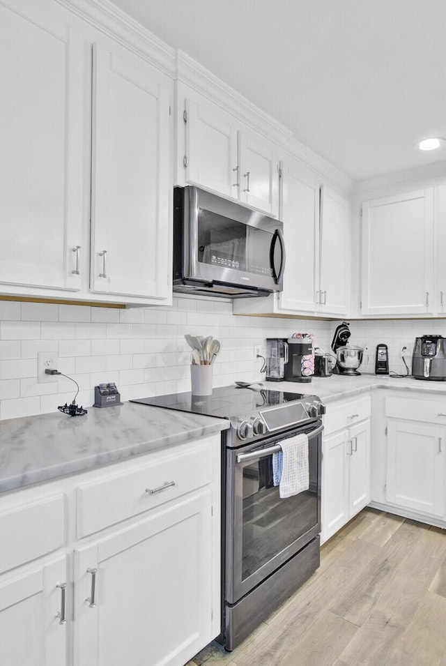 kitchen with stainless steel appliances, tasteful backsplash, light stone countertops, and white cabinets