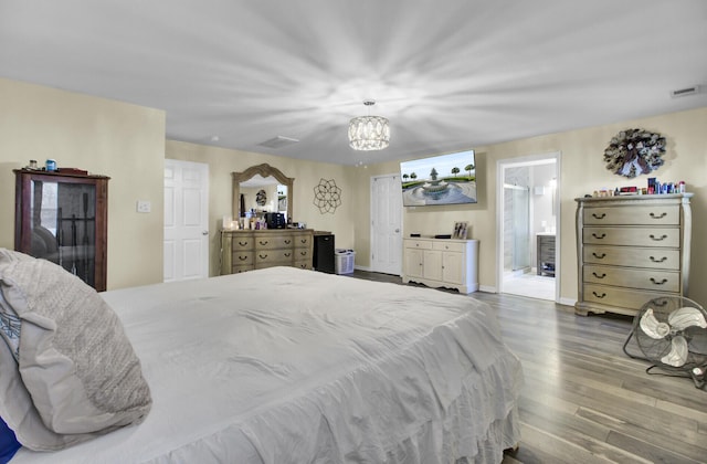 bedroom with connected bathroom, a notable chandelier, and light hardwood / wood-style floors