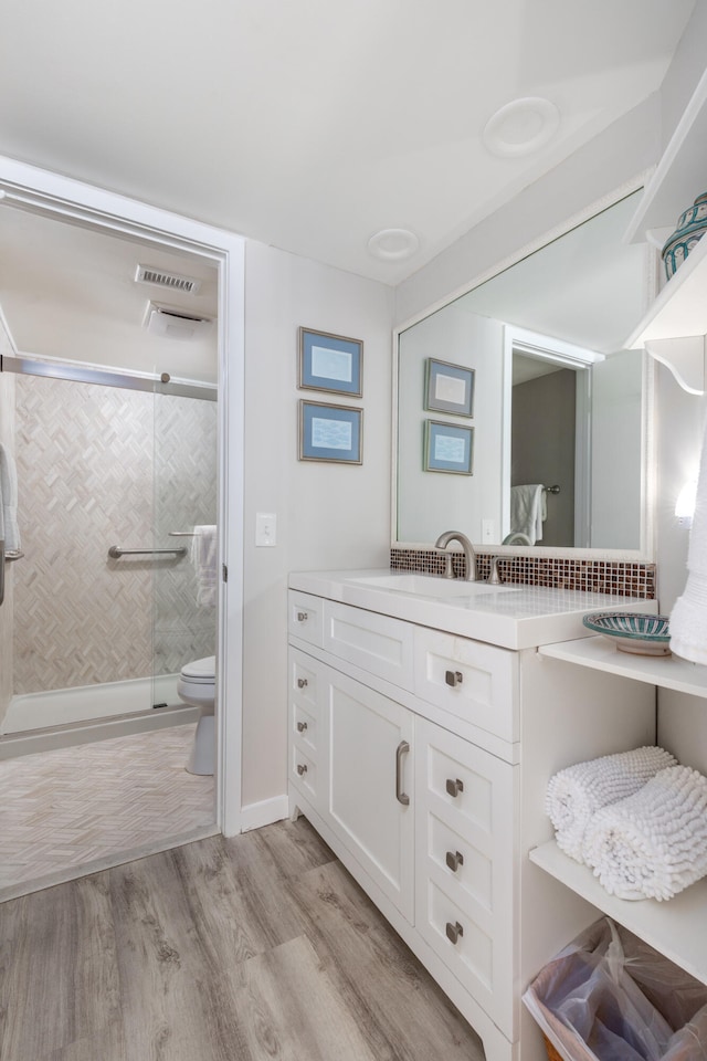 bathroom with wood-type flooring, an enclosed shower, backsplash, vanity, and toilet