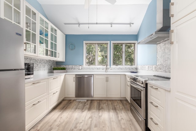 kitchen featuring white cabinetry, appliances with stainless steel finishes, wall chimney range hood, and tasteful backsplash