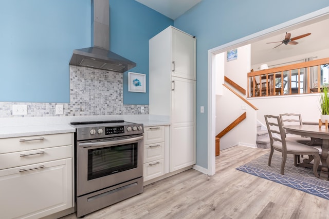 kitchen featuring light wood-type flooring, wall chimney range hood, stainless steel electric range, and white cabinets