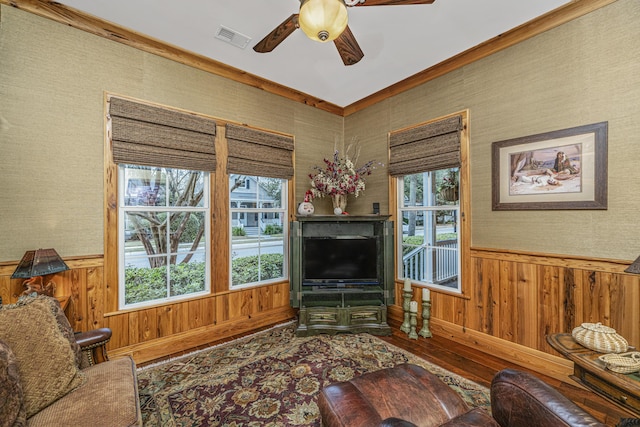 living room featuring hardwood / wood-style flooring, crown molding, ceiling fan, and wooden walls