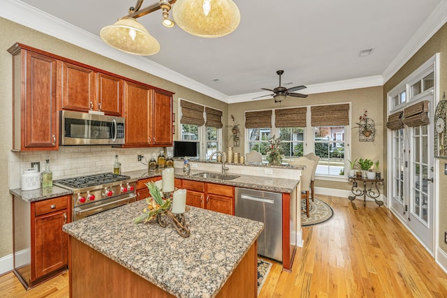 kitchen with a center island, sink, stainless steel appliances, light stone counters, and light hardwood / wood-style floors