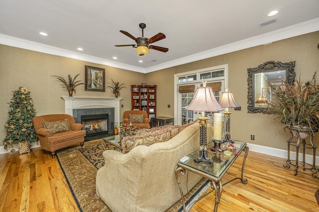 living room featuring hardwood / wood-style flooring, crown molding, and a tiled fireplace