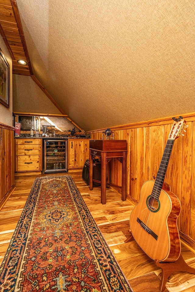 additional living space with vaulted ceiling, beverage cooler, a textured ceiling, and light wood-type flooring