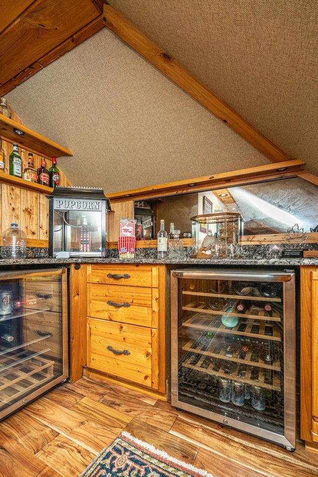 bar featuring light wood-type flooring, lofted ceiling with beams, wine cooler, and dark stone counters