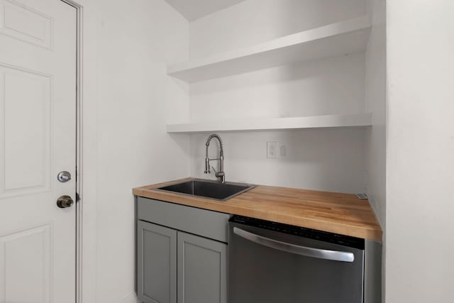 kitchen with gray cabinetry, sink, stainless steel dishwasher, and wooden counters