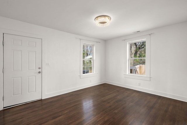 spare room featuring a healthy amount of sunlight and dark hardwood / wood-style flooring