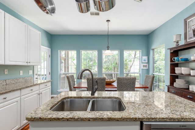 kitchen featuring white cabinets, light stone countertops, hanging light fixtures, and a sink