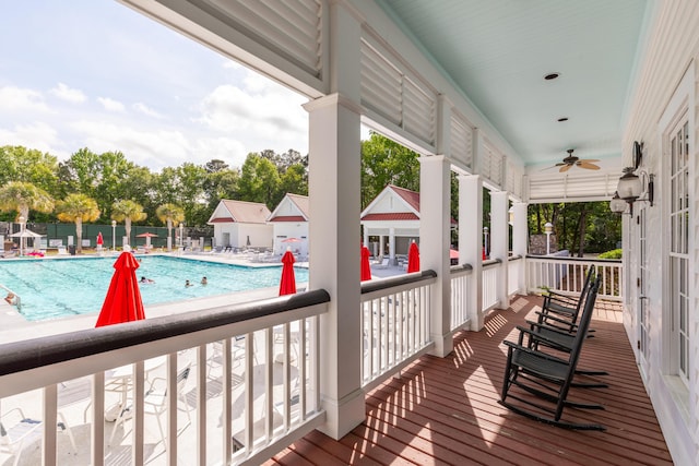wooden deck with a ceiling fan, a community pool, a patio area, and fence