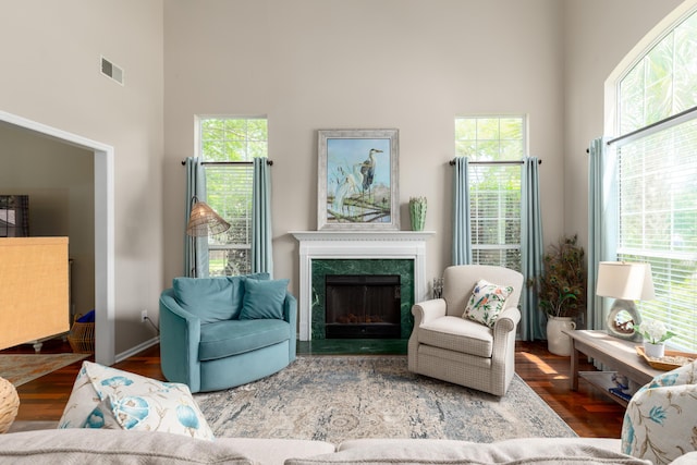living room with a premium fireplace, a high ceiling, visible vents, and wood finished floors