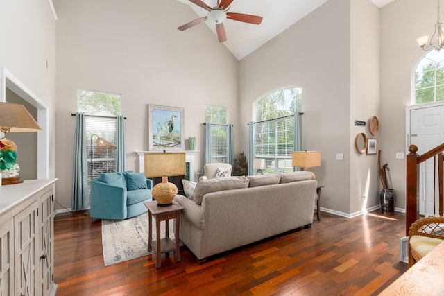 living area with a fireplace, high vaulted ceiling, dark wood finished floors, ceiling fan with notable chandelier, and baseboards