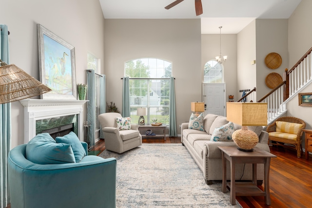 living area featuring wood finished floors, stairs, a towering ceiling, and ceiling fan with notable chandelier