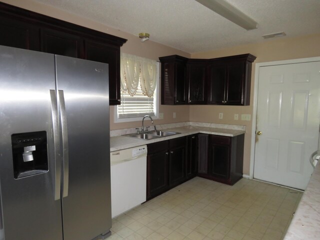kitchen featuring stainless steel refrigerator with ice dispenser, dishwasher, a sink, light countertops, and light floors