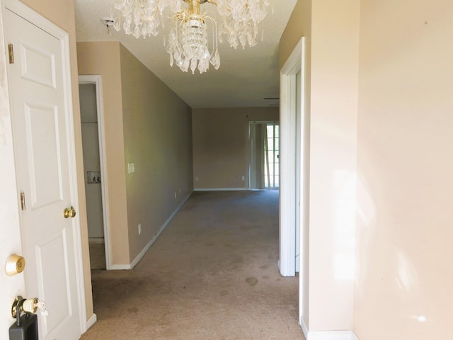 hallway with a chandelier, light colored carpet, and baseboards