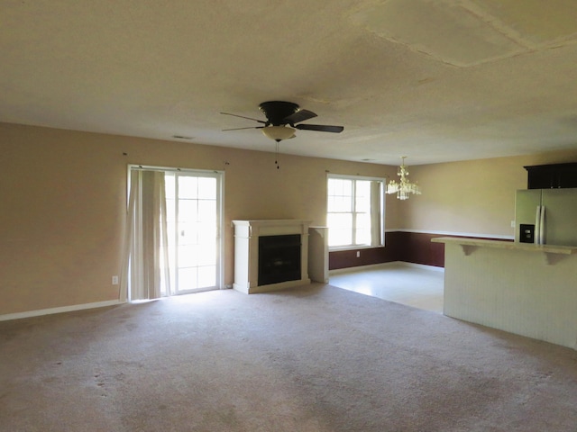 unfurnished living room with ceiling fan, a chandelier, a fireplace, light colored carpet, and baseboards