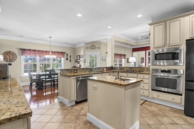 kitchen featuring cream cabinets, crown molding, appliances with stainless steel finishes, a sink, and a peninsula