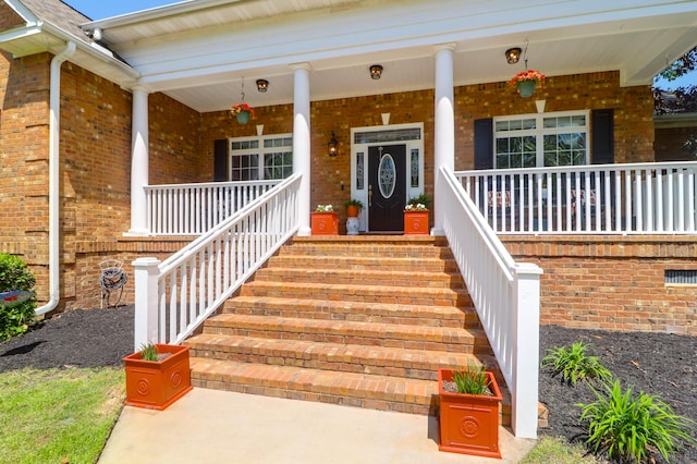 doorway to property featuring covered porch and brick siding