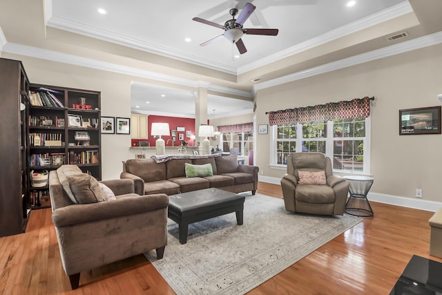 living area with visible vents, ceiling fan, wood finished floors, and a tray ceiling