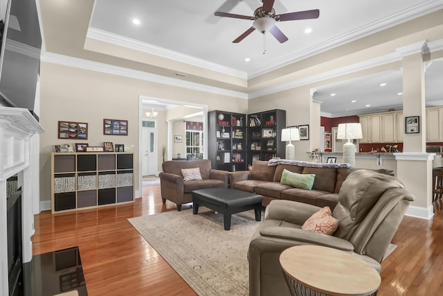 living area featuring visible vents, a fireplace with flush hearth, wood finished floors, ceiling fan with notable chandelier, and a tray ceiling