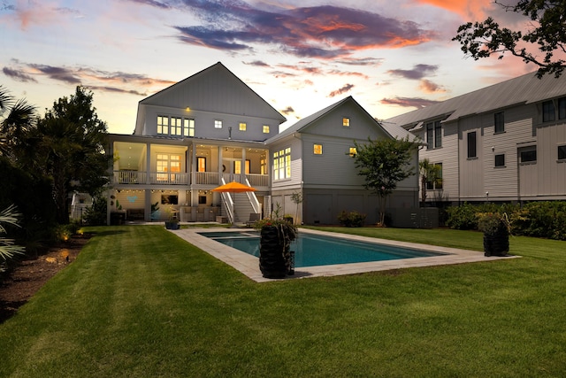566 Wading Pl, Daniel Island, SC 29492 - back of house at dusk with stairway, a lawn, an outdoor pool, ceiling fan, and board and batten siding