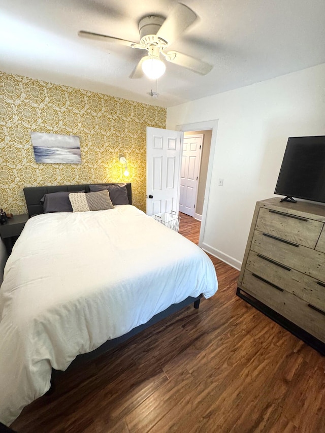 bedroom with a ceiling fan, wallpapered walls, dark wood finished floors, and baseboards